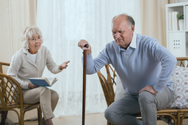 Older man with walking stick suffering with severe knee pain from arthritis