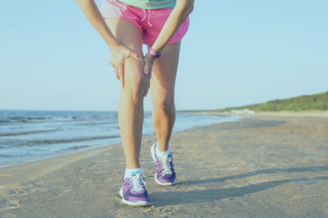 Woman running on the beach holding her knee in pain